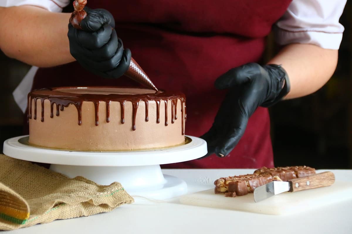 Cake decorator adding chocolate drip to a cake.