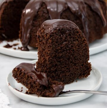 Close up featured image of a moist chocolate cake on a white plate with a fork.