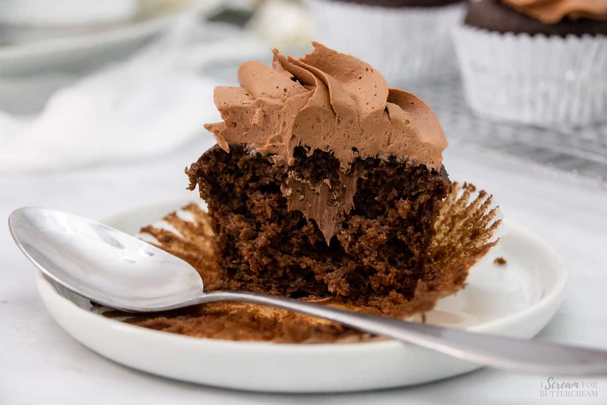 Wide image of chocolate cupcake cut open and filled on a white plate with a spoon.
