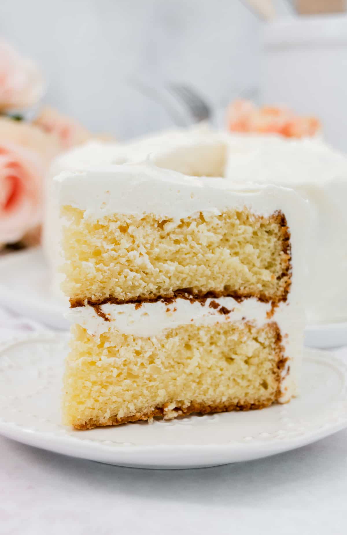 Large slice of layer vanilla cake with vanilla frosting on a white plate.