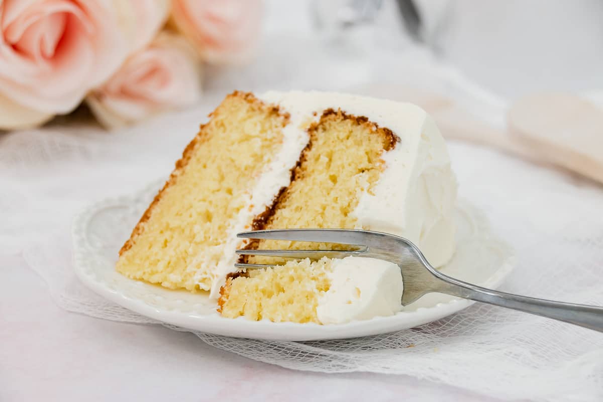 Wide image of layer cake in vanilla flavor on a plate with a fork.