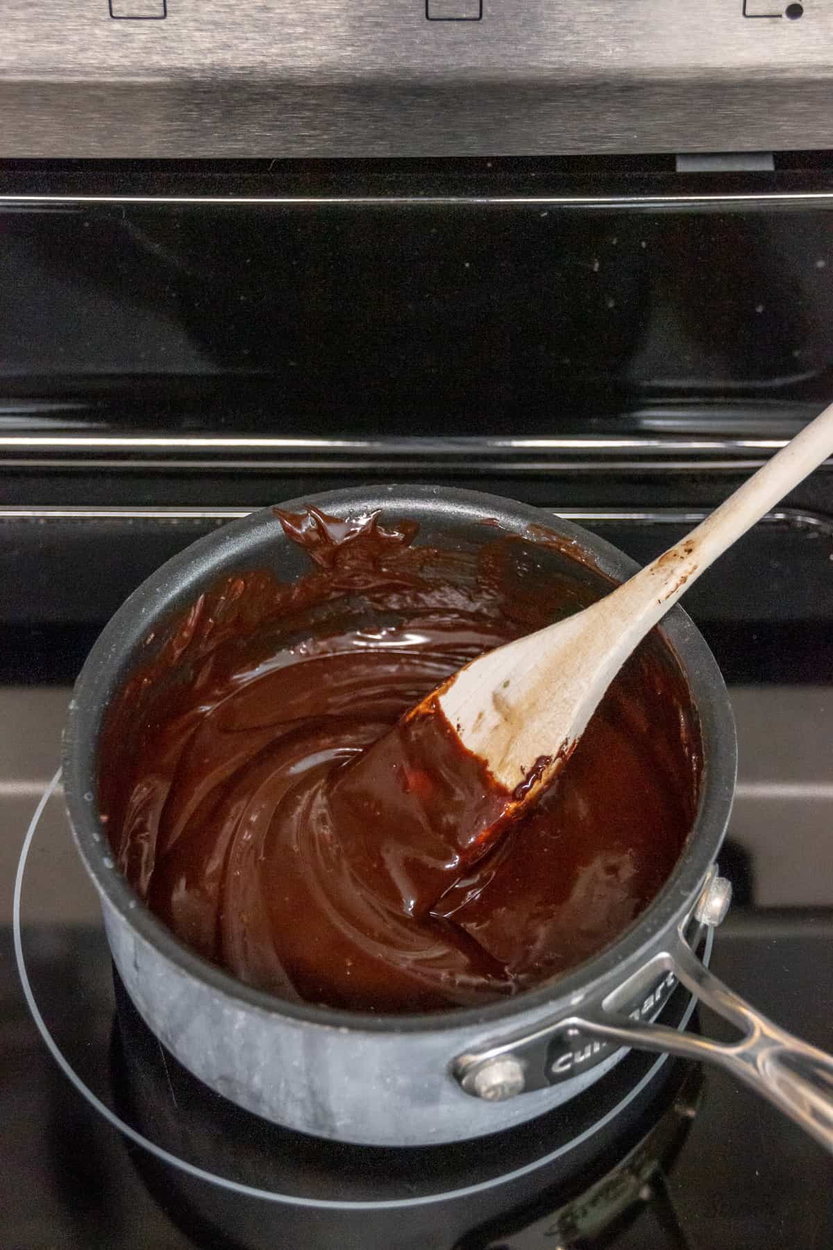 Melted chocolate and cream in a saucepan with a wooden spoon.