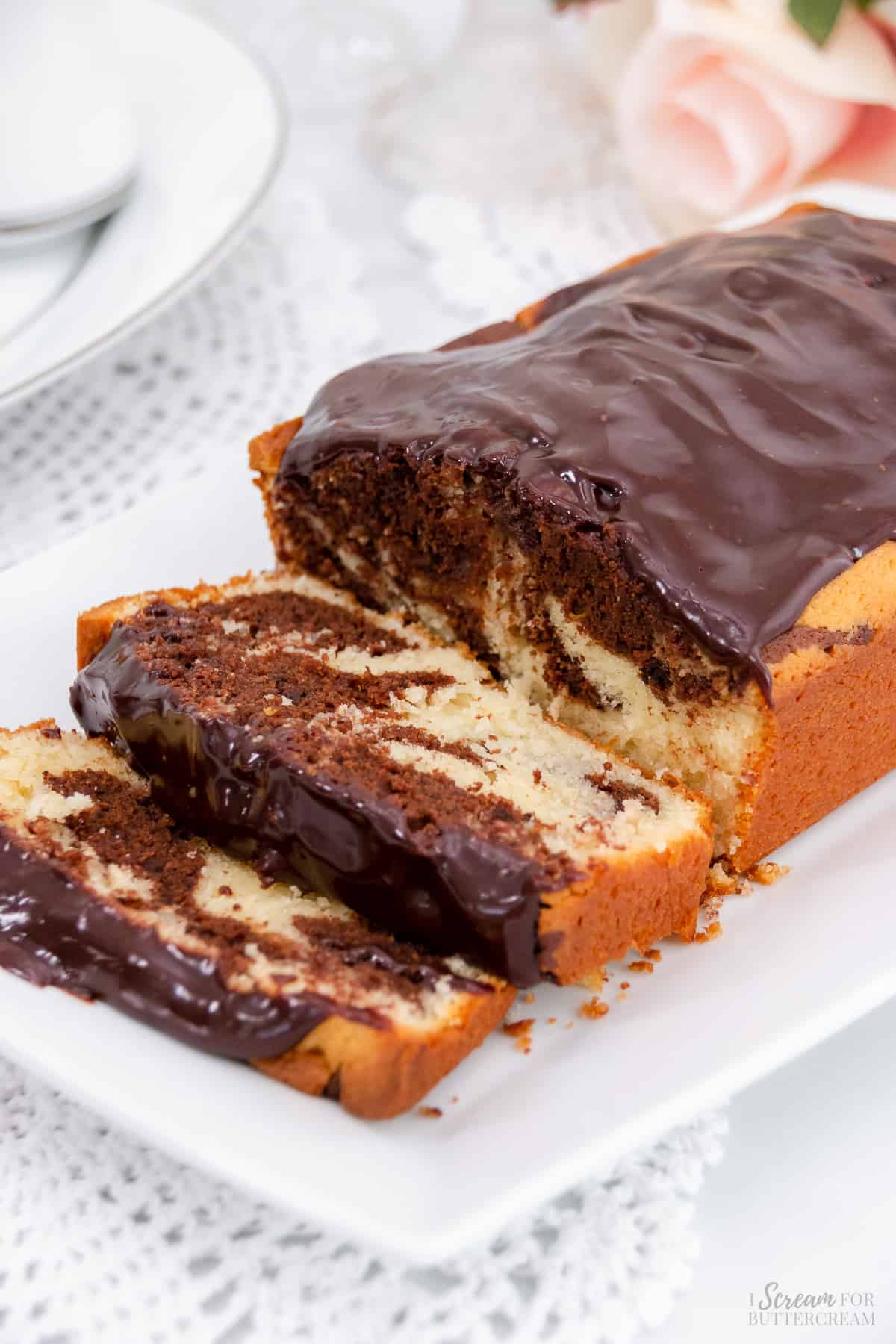 Tall image of sliced and glazed marble loaf cake on a white platter.