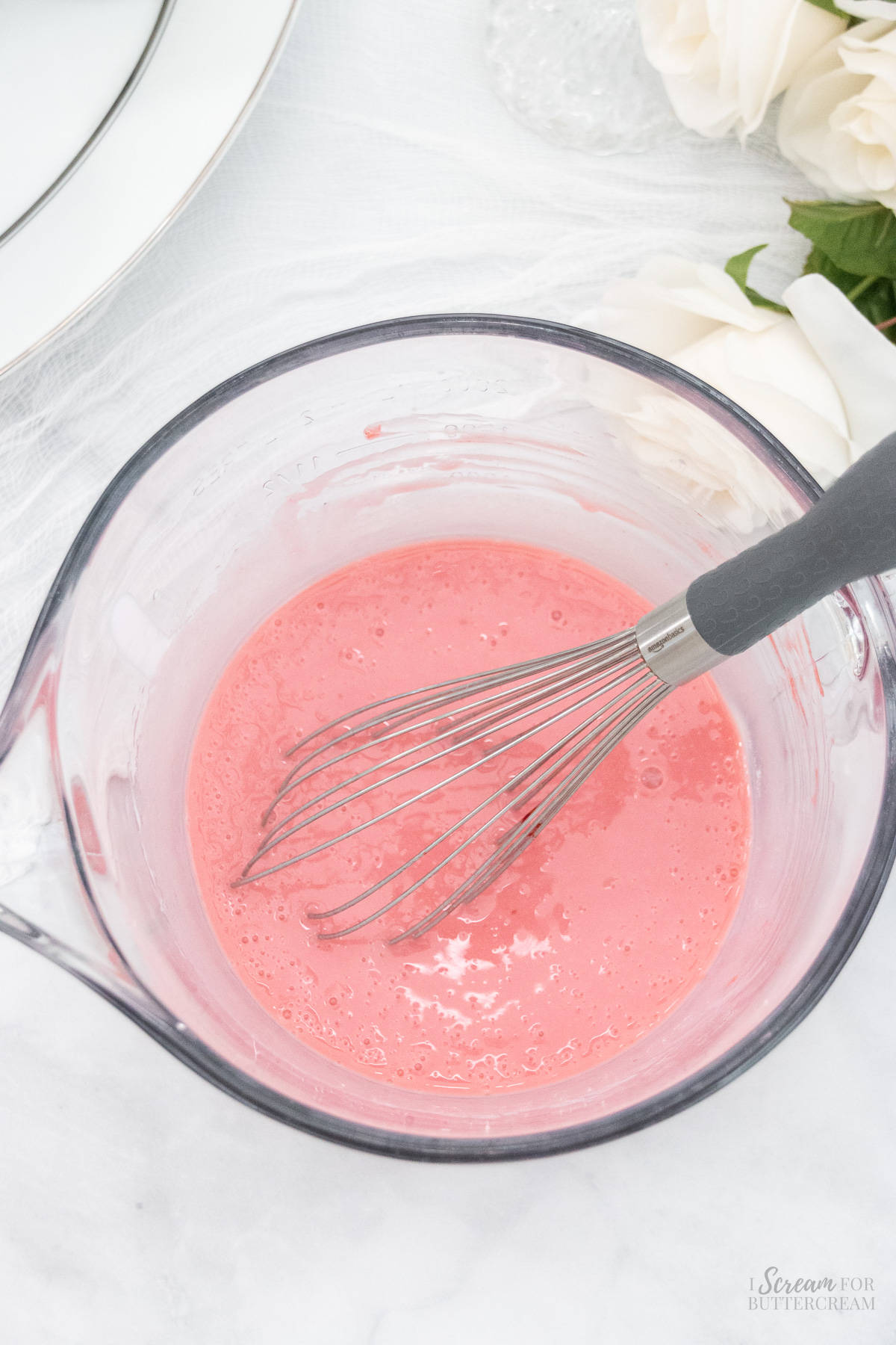 Liquid cake ingredients in a glass bowl with a whisk.