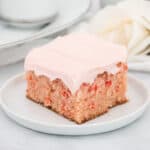 Slice of moist cherry vanilla cake on a white plate with frosting.