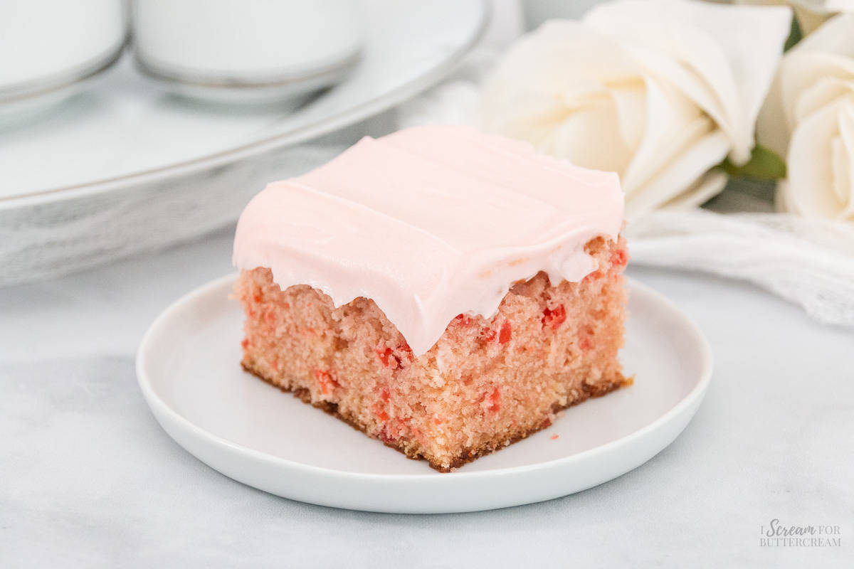 Slice of moist cherry vanilla cake on a white plate with frosting.