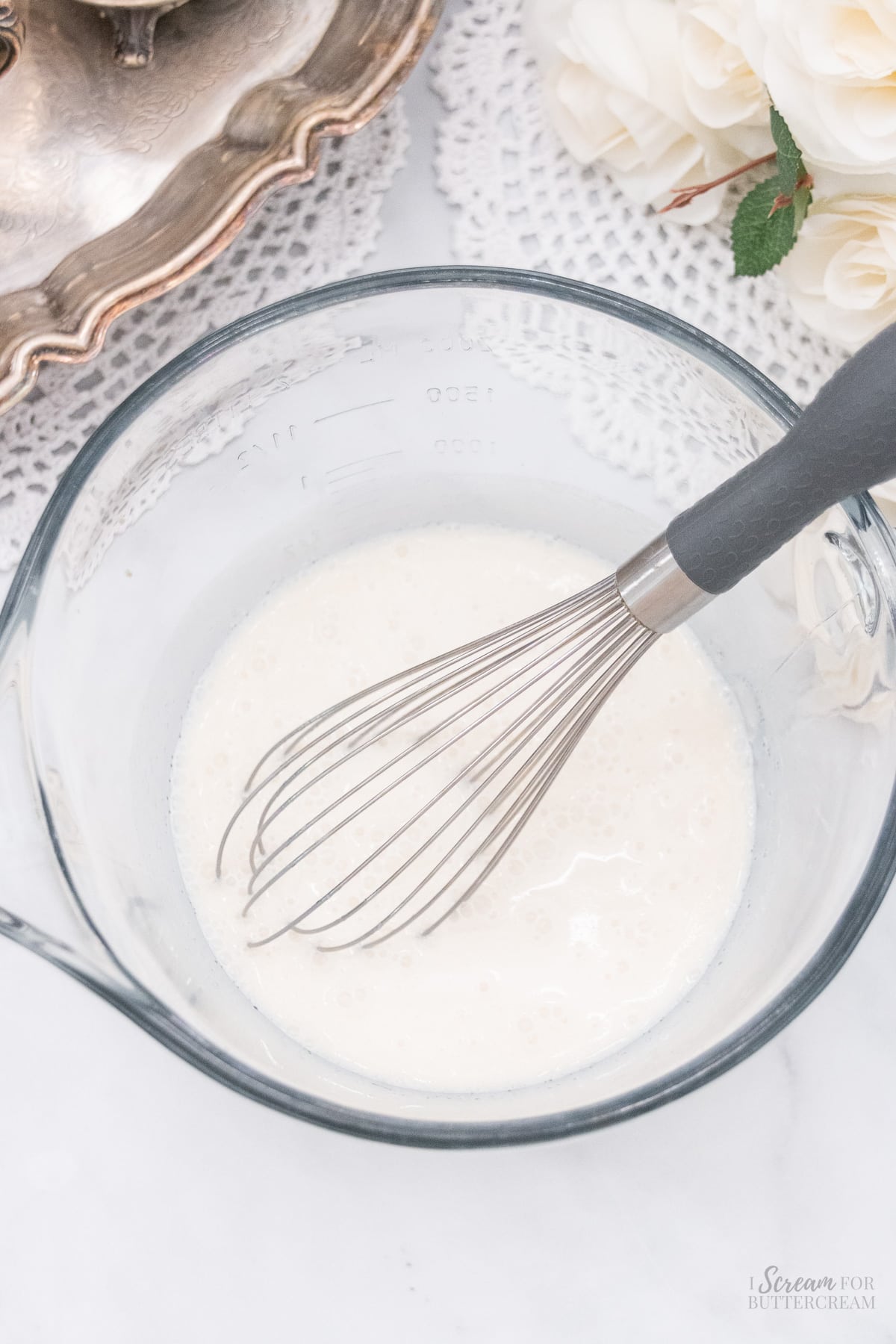 Liquid cake batter ingredients on a glass bowl with a whisk.