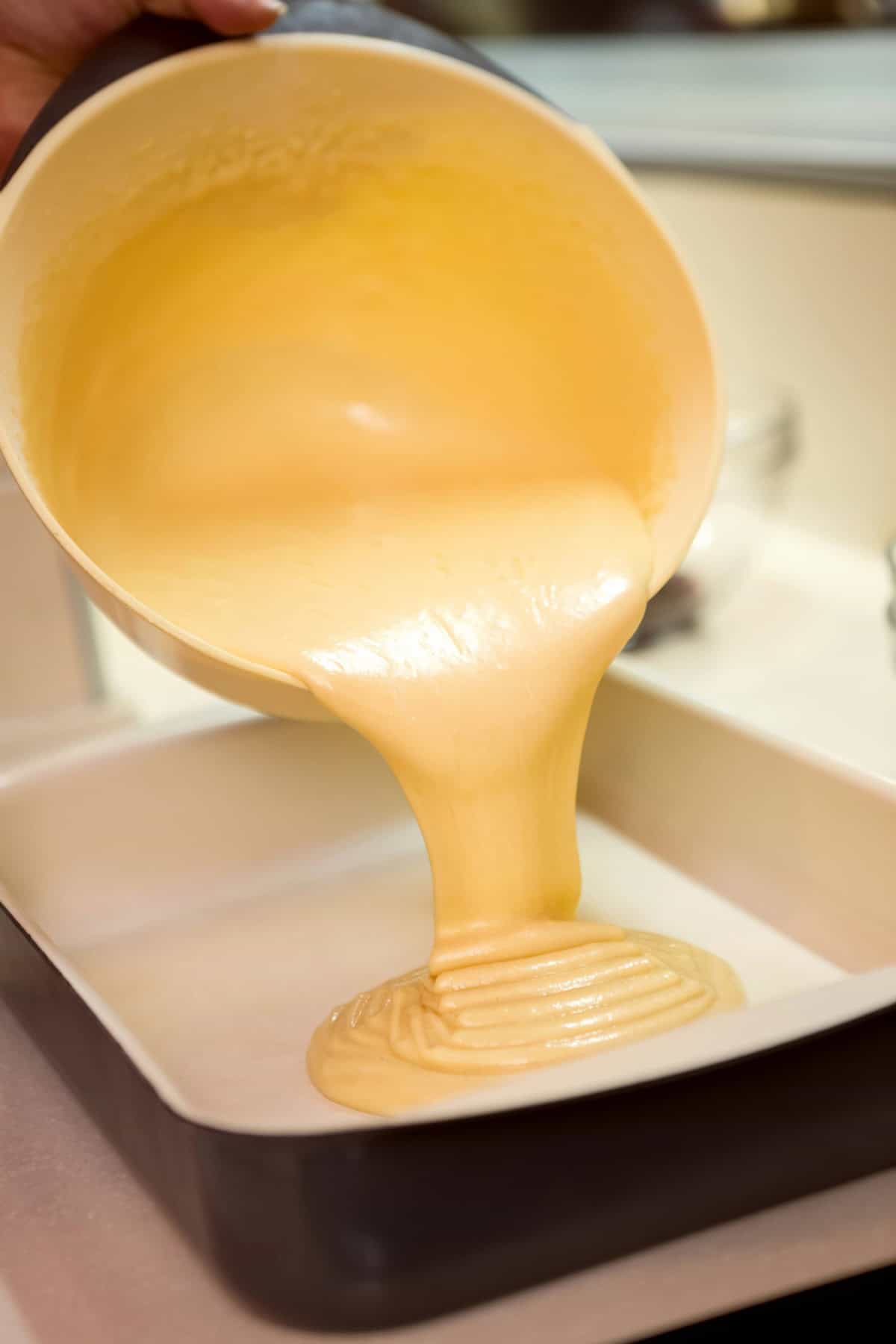 Cake batter being poured into a square cake pan.