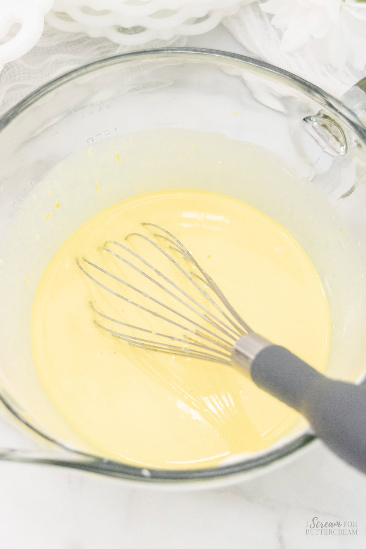 Liquid cake ingredients in a glass bowl with a whisk.
