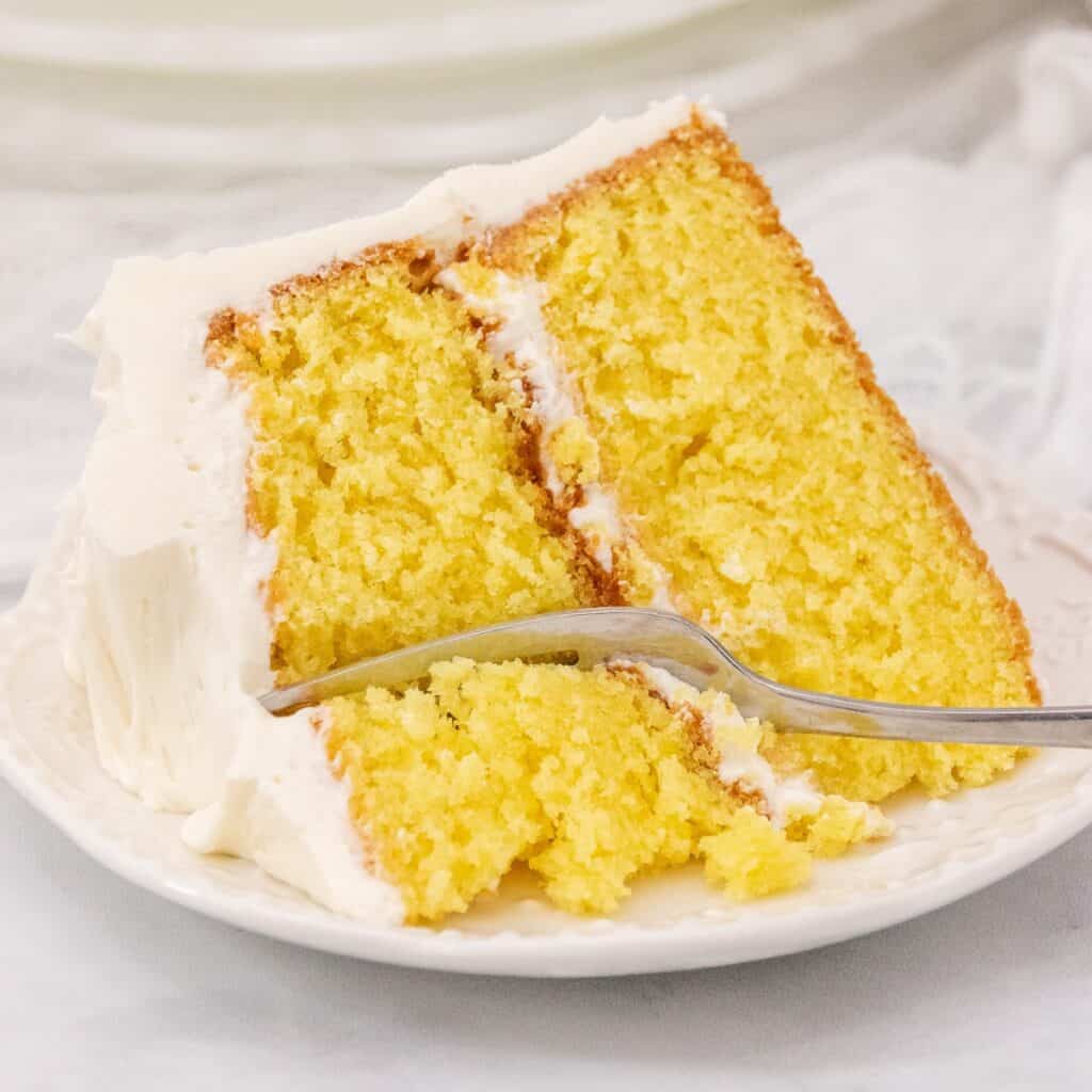 Close up image of moist lemon sour cream layer cake on a white plate with a fork.