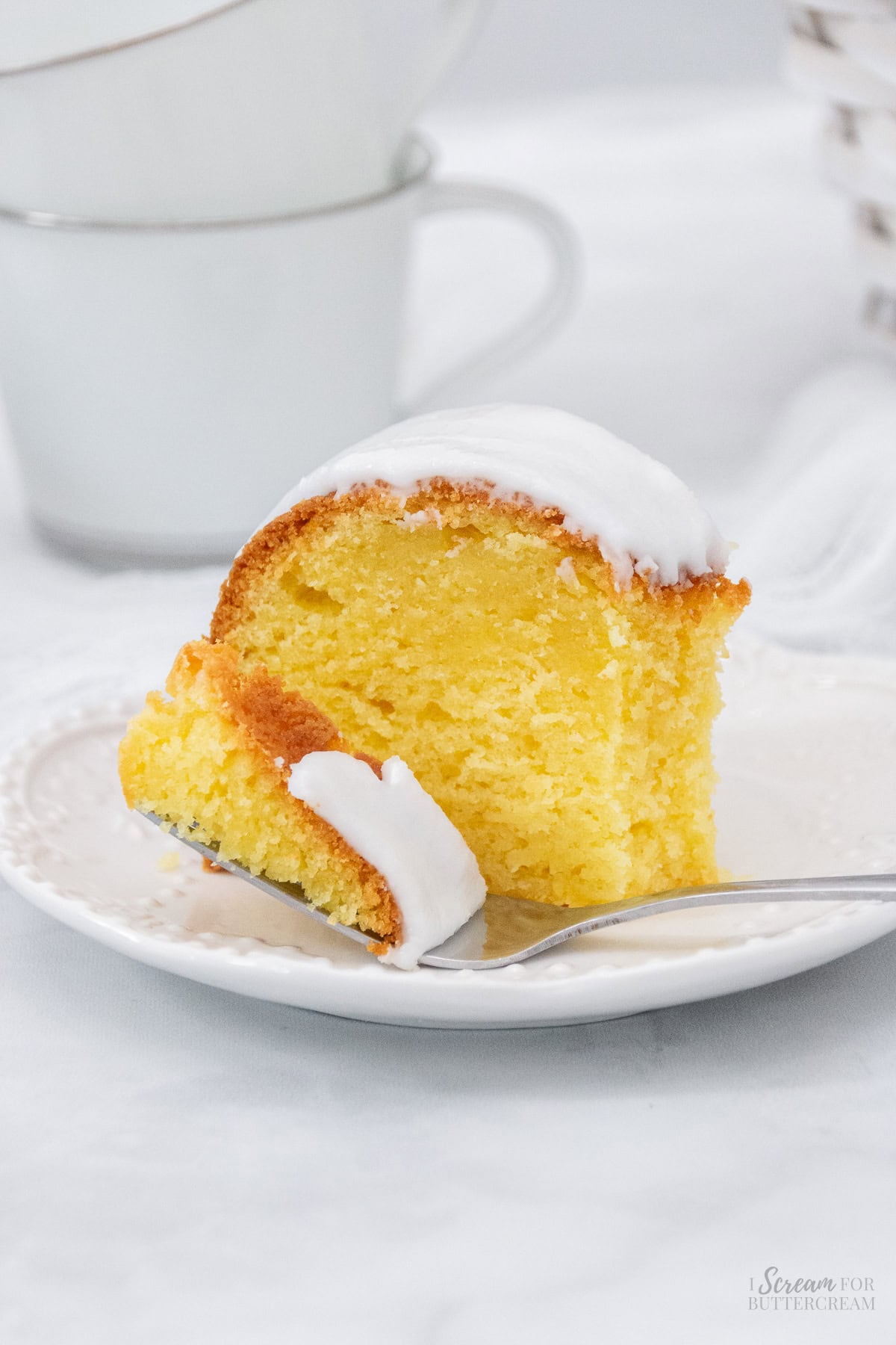 Close up of lemon cream cheese cake with fork on a white plate.