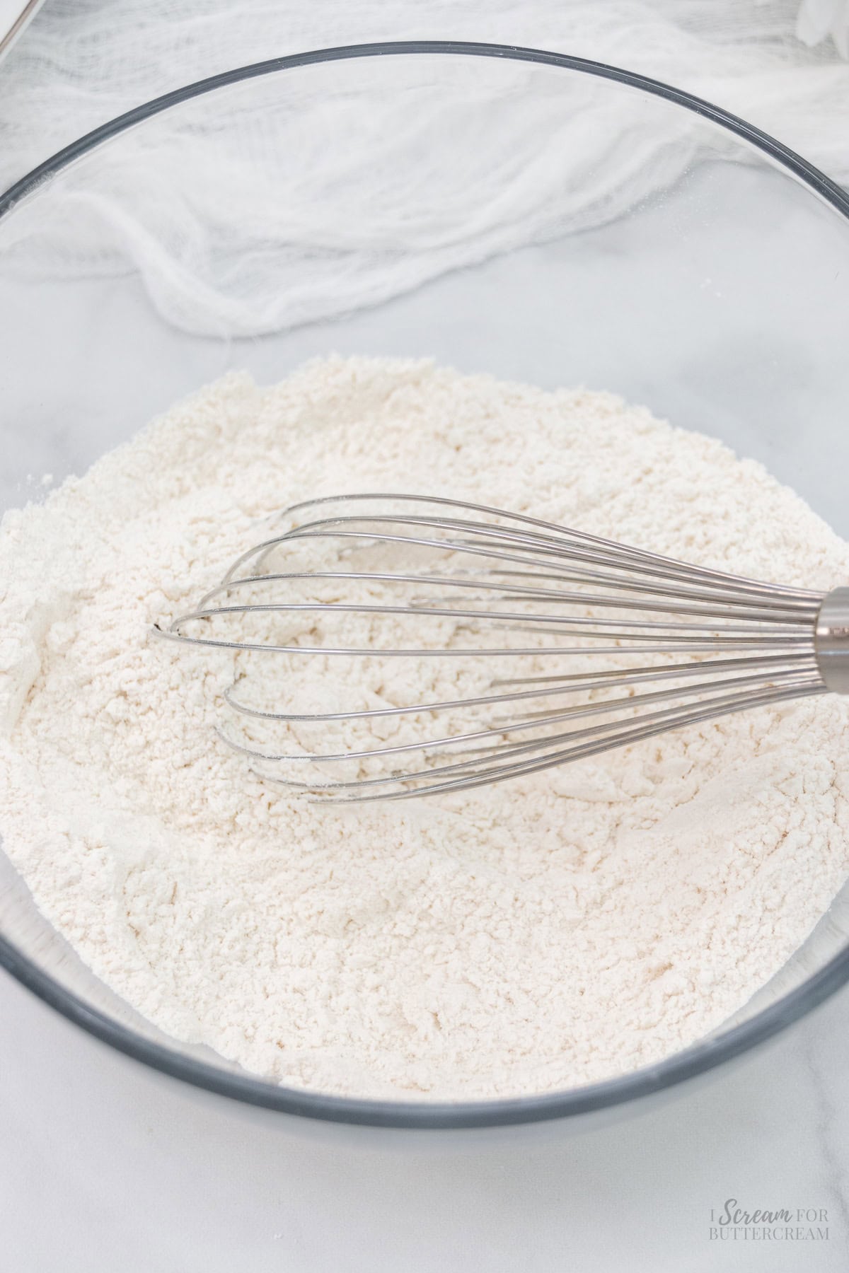 Dry cake ingredients in a glass mixing bowl with a whisk.