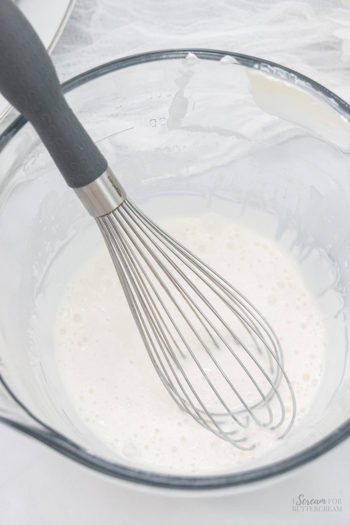 Liquid cake batter ingredients in a glass bowl with a whisk.