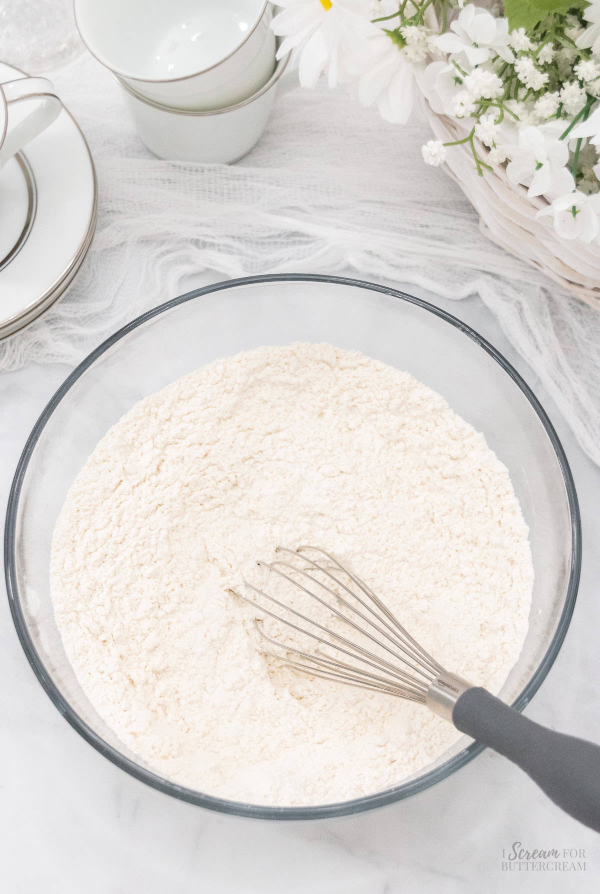 Dry cake batter ingredients in a glass mixing bowl with a whisk.