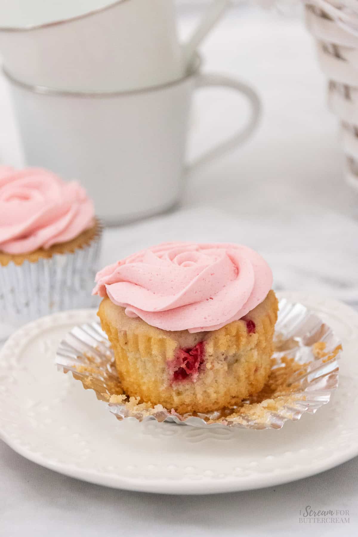 Close up image of a raspberry vanilla cupcake with frosting on a white plate.