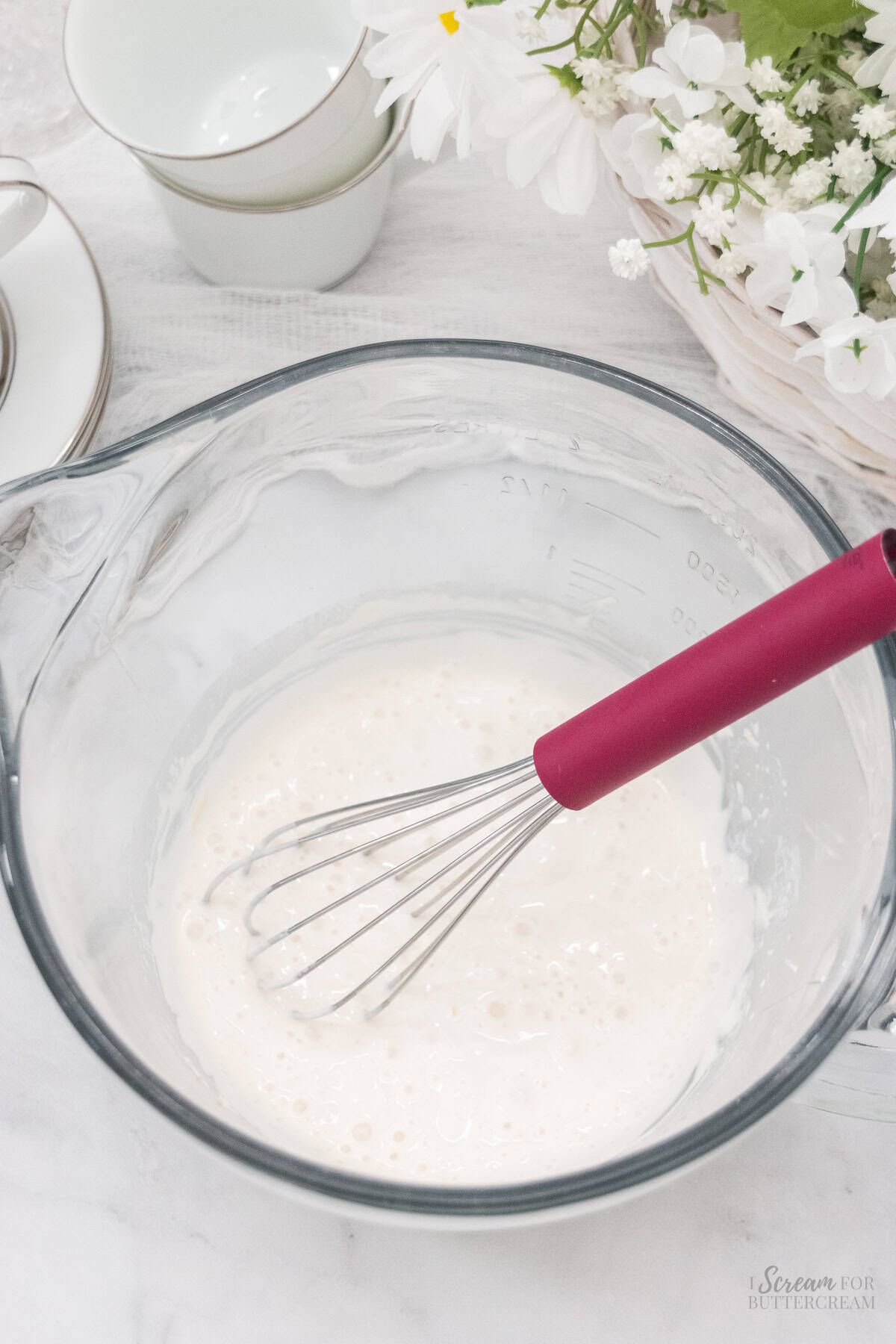 Liquid cake batter ingredients in a glass mixing bowl with a whisk.