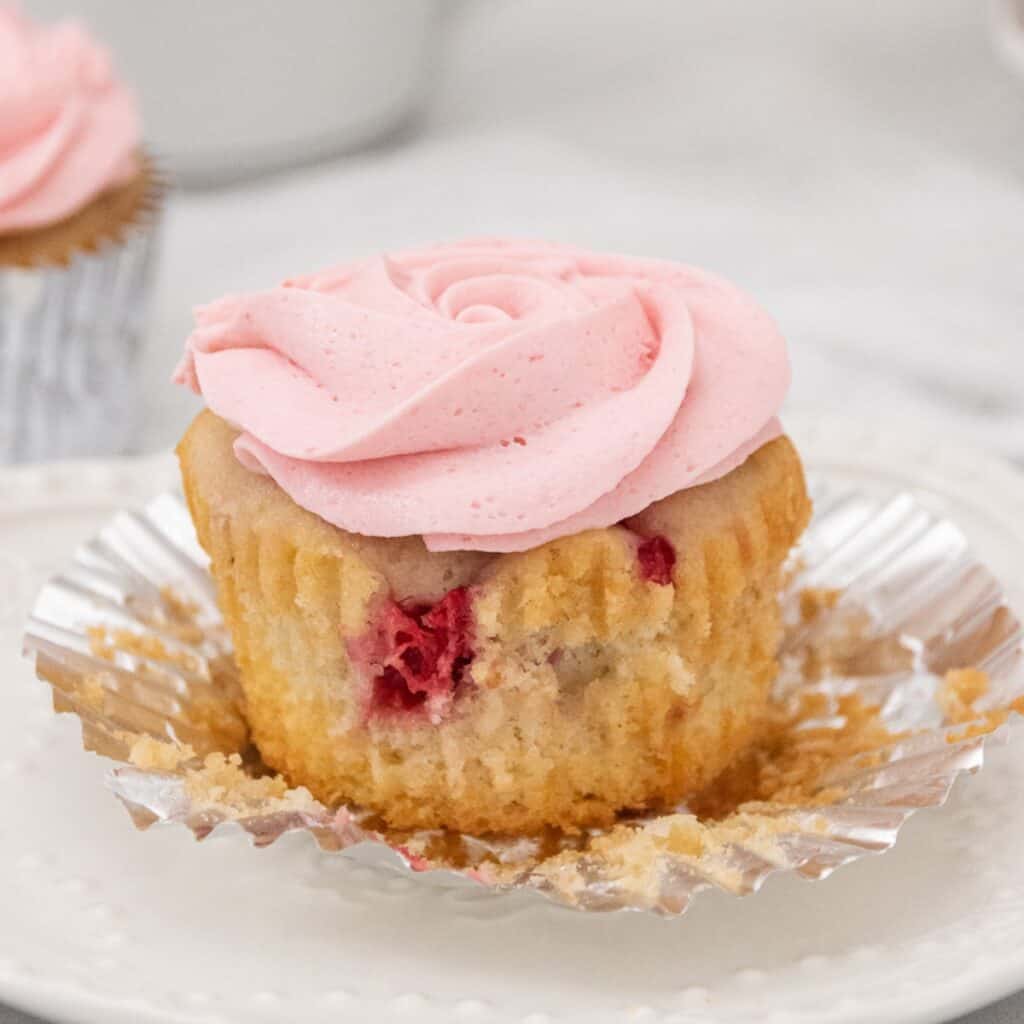 Close up view of raspberry cupcake on a white plate with pink swirl icing.