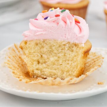 Featured image of cut vanilla cupcake with pink icing on a white plate.