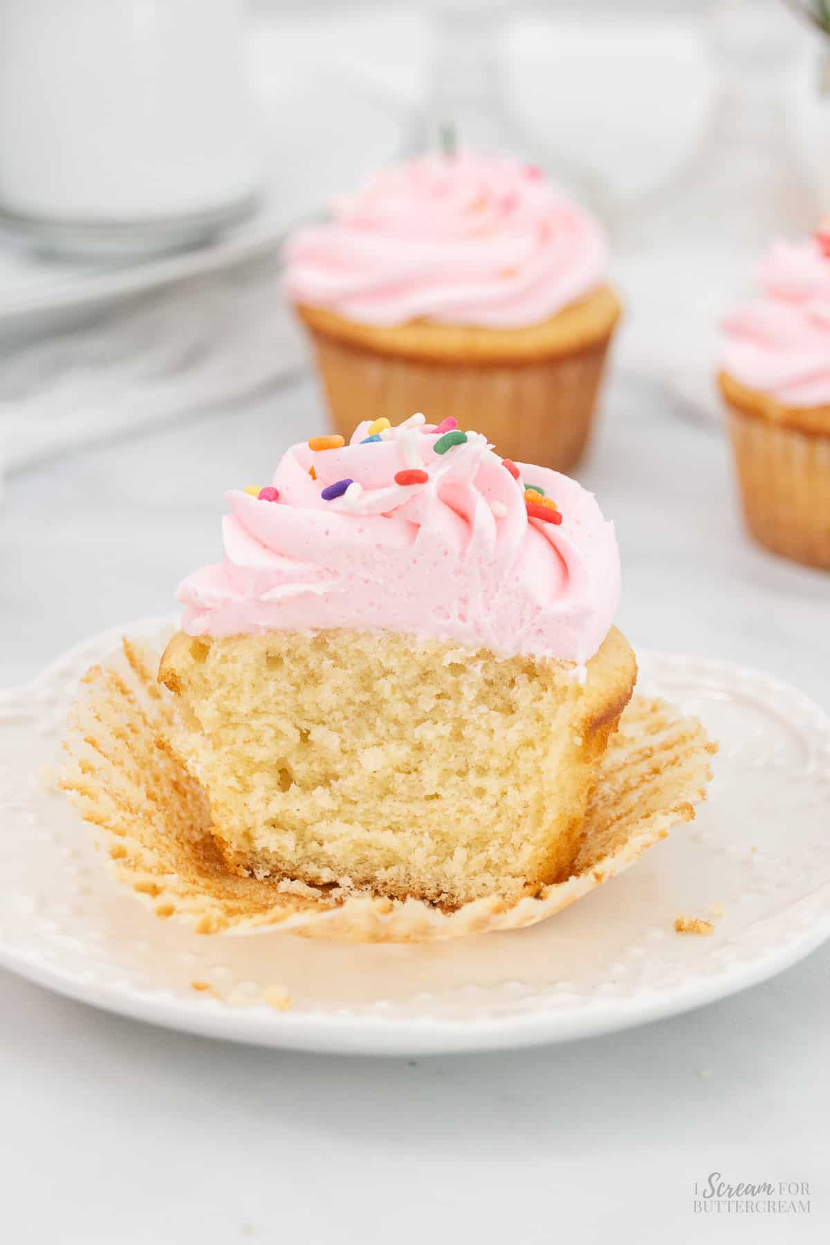 Cut vanilla sour cream cupcake with frosting and sprinkles on a white plate.