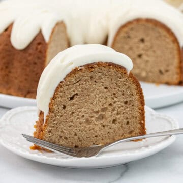 Large slice of spice cake with glaze on a white plate with a fork.