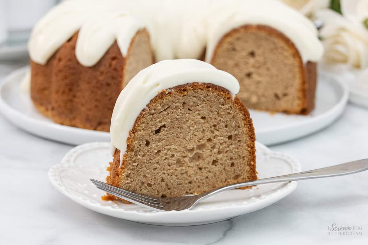 Large slice of spice cake with glaze on a white plate with a fork.