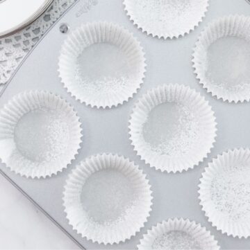 A clean cupcake pan filled with white liners that have been lightly sprayed with nonstick cooking spray, ready for baking.