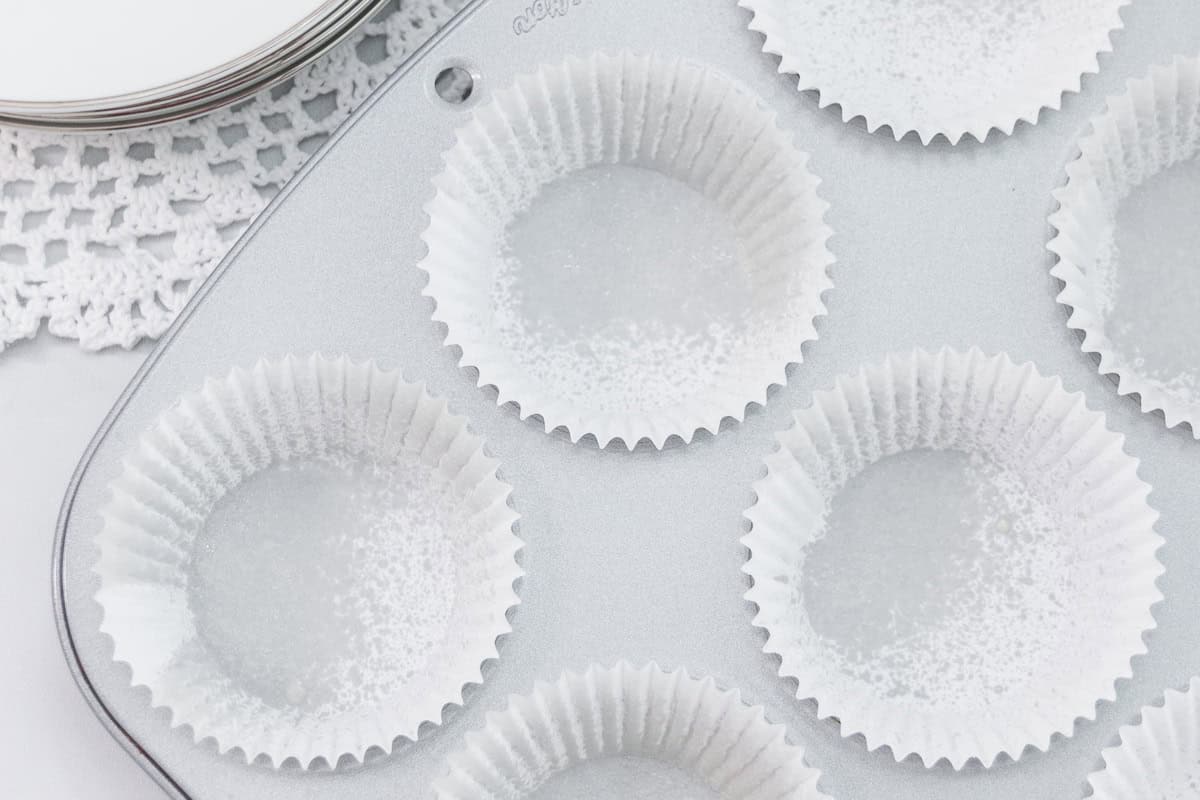 A clean cupcake pan filled with white liners that have been lightly sprayed with nonstick cooking spray, ready for baking.