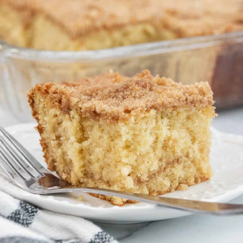 A slice of buttermilk coffee cake with a crumbly cinnamon-sugar topping on a white plate with a fork.