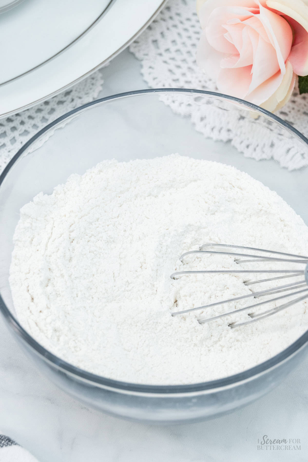 A glass bowl with dry ingredients and a whisk, ready to be combined for baking.