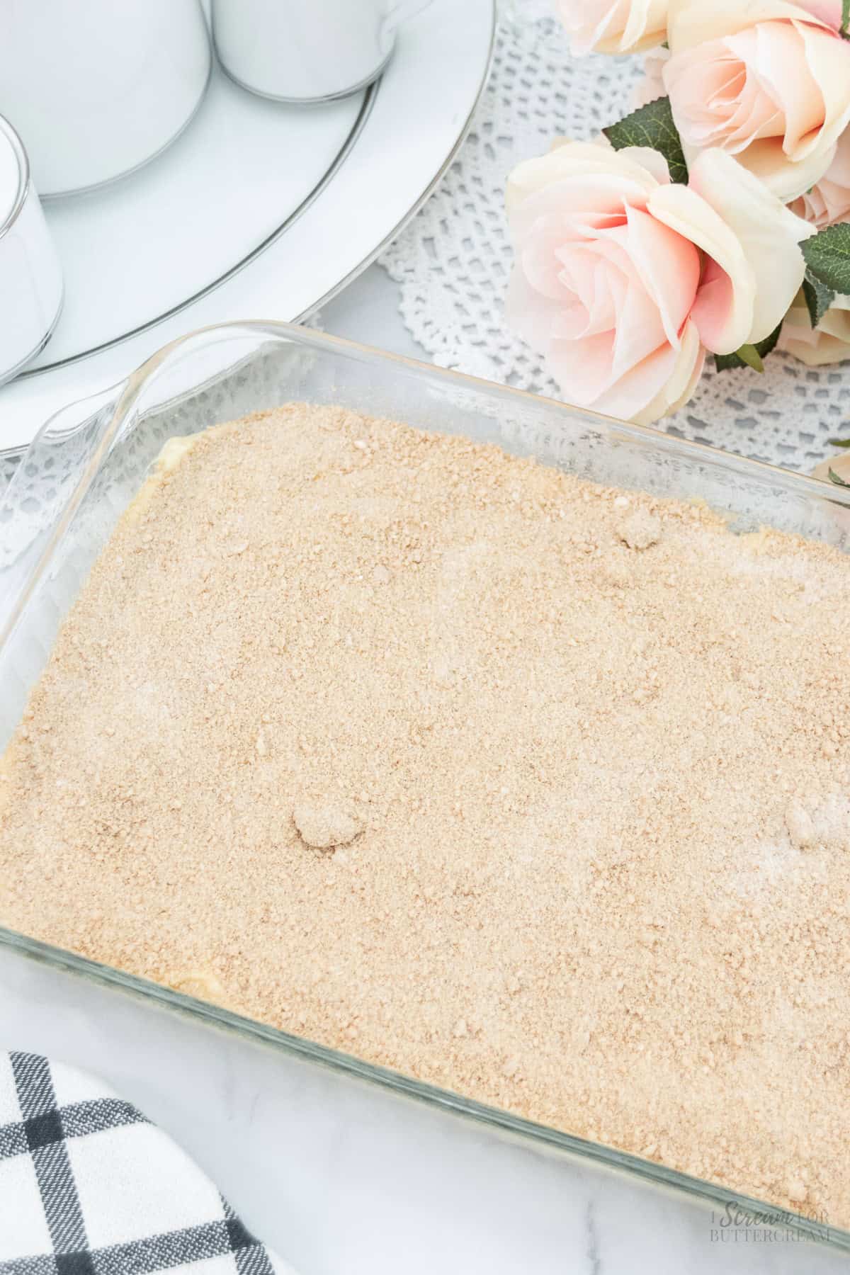 A glass baking dish filled with cake batter topped with a layer of cinnamon-sugar mixture, ready to be baked.