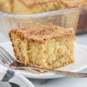 A slice of moist buttermilk coffee cake with a cinnamon-sugar topping, served on a white plate with a fork.