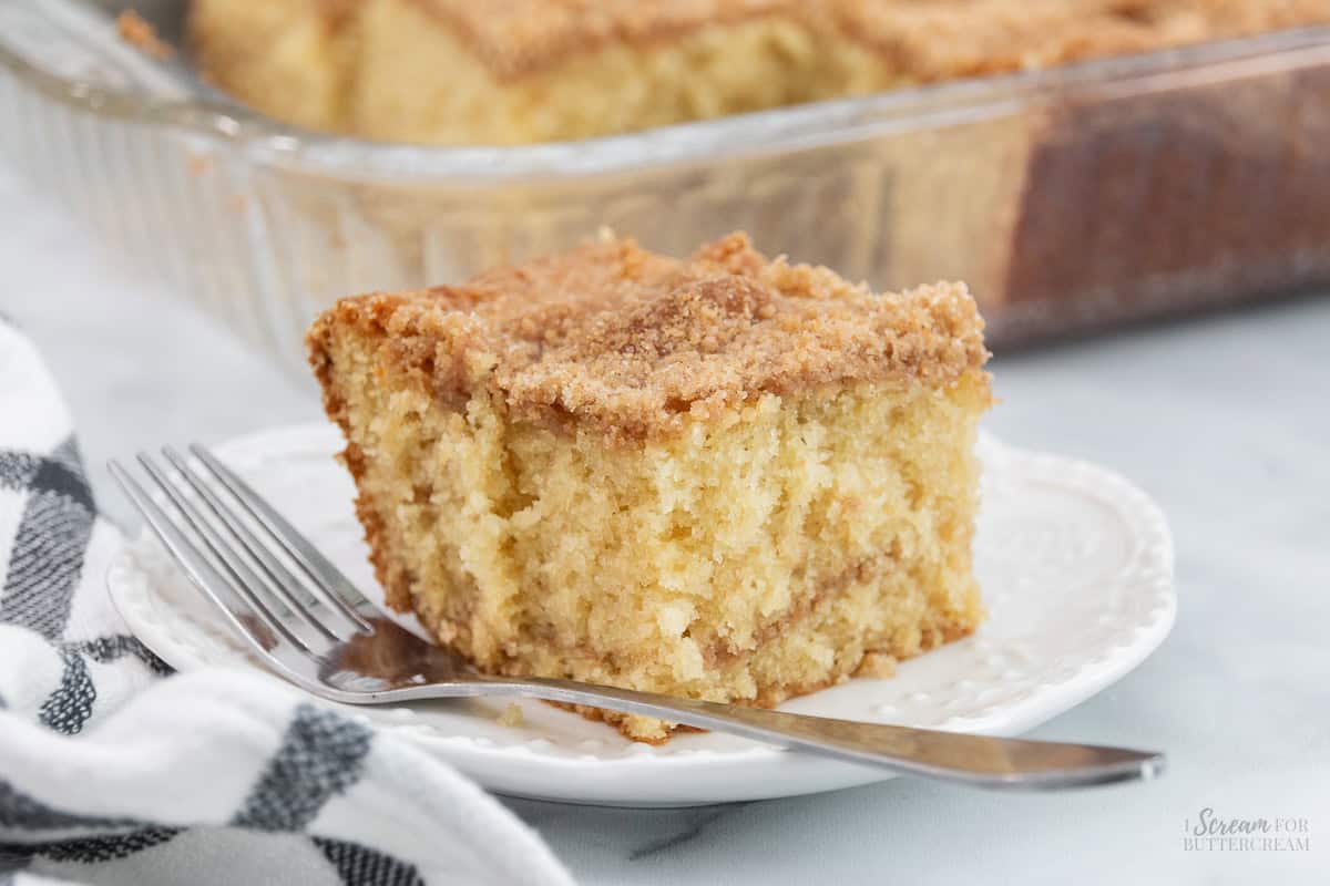 A slice of moist buttermilk coffee cake with a cinnamon-sugar topping, served on a white plate with a fork.