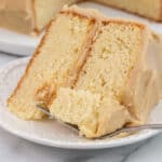 A wide shot of a single slice of caramel cake on a white plate, featuring fluffy golden layers and smooth caramel frosting, with a forkful of cake resting on the plate for an inviting touch.