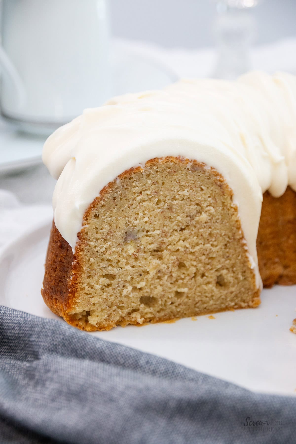 Side view of a frosted banana pound cake on a white plate, showing the full texture and golden brown crust.