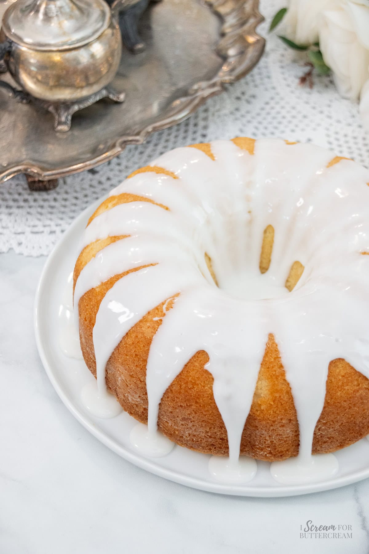 Golden coconut pound cake with thick white glaze dripping down the sides on a white plate.