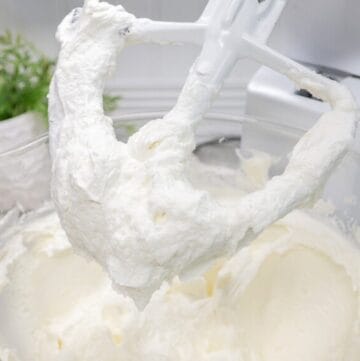 "Close-up of a stand mixer paddle attachment covered in fluffy, whipped buttercream frosting over a mixing bowl.