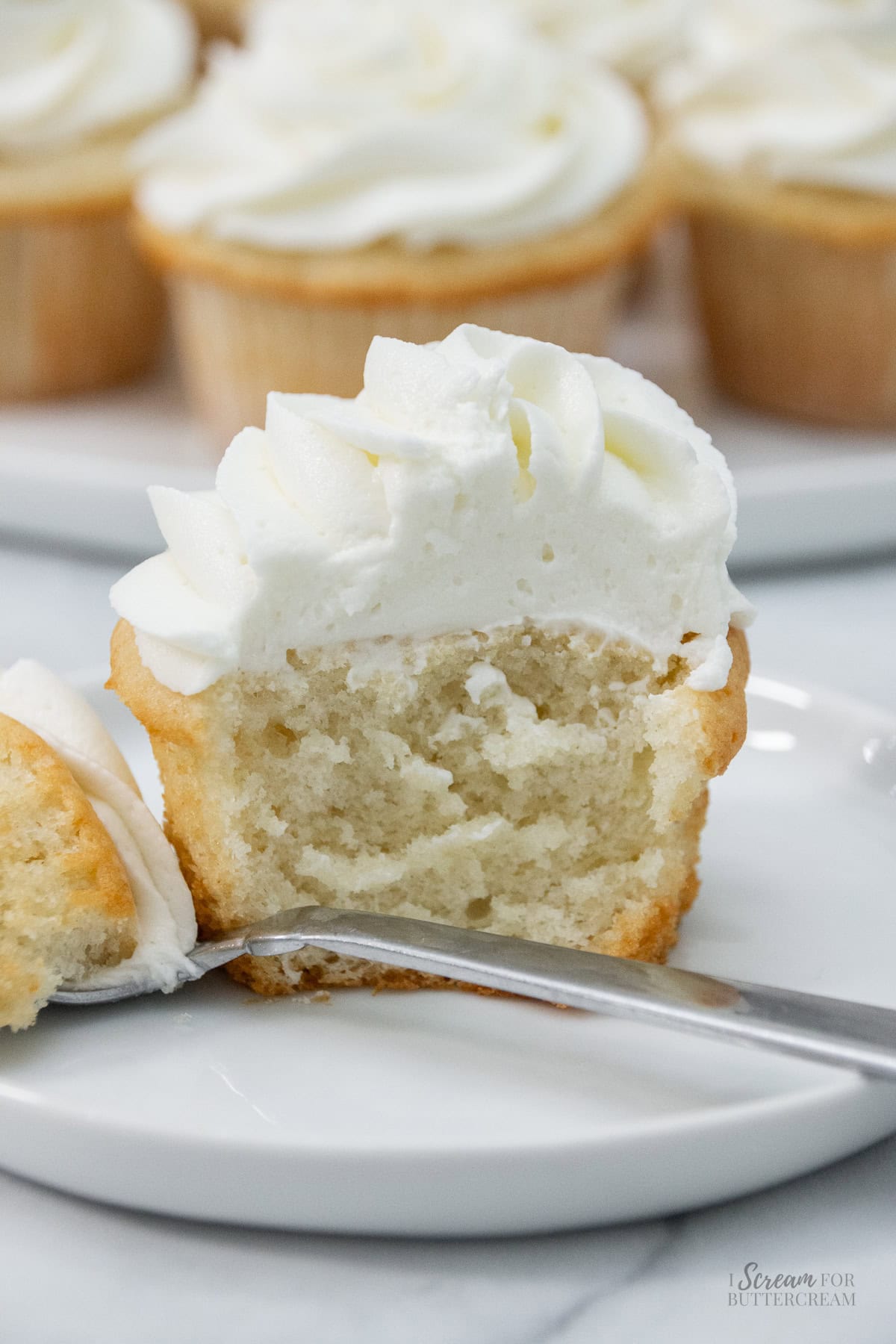 Sour cream white cupcake sliced in half on a plate, showing its soft crumb and topped with a swirl of white frosting.