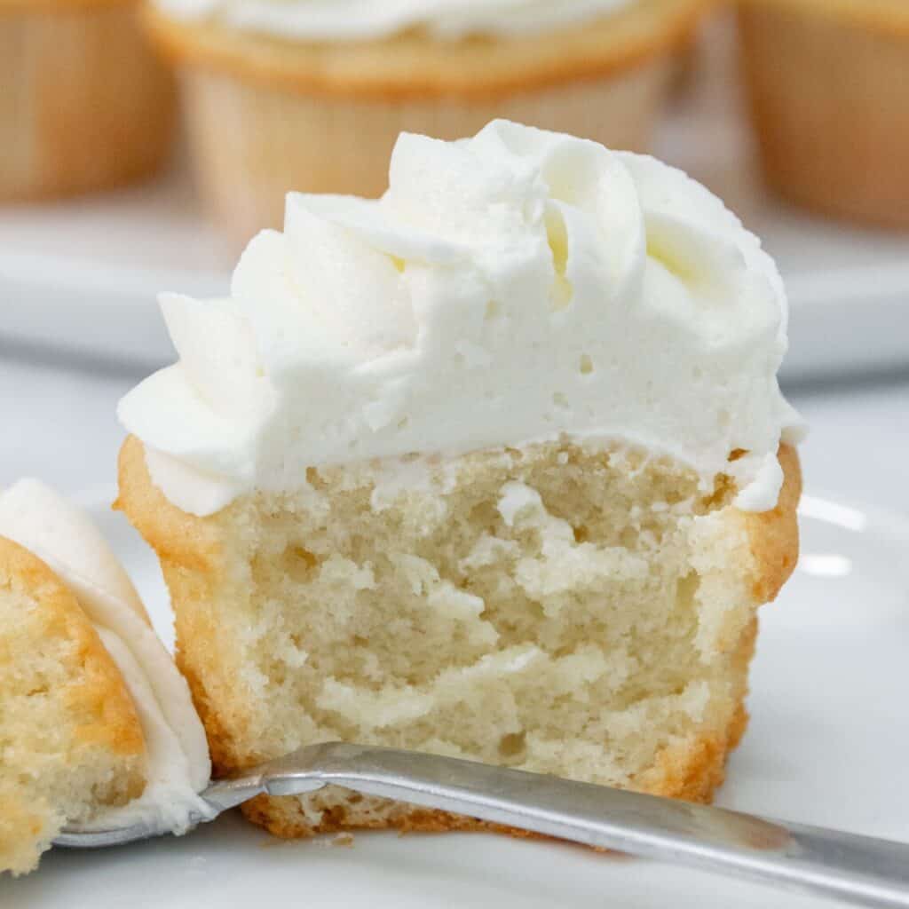 Close-up of a vanilla cupcake with fluffy white frosting, cut in half to show its soft, moist crumb.