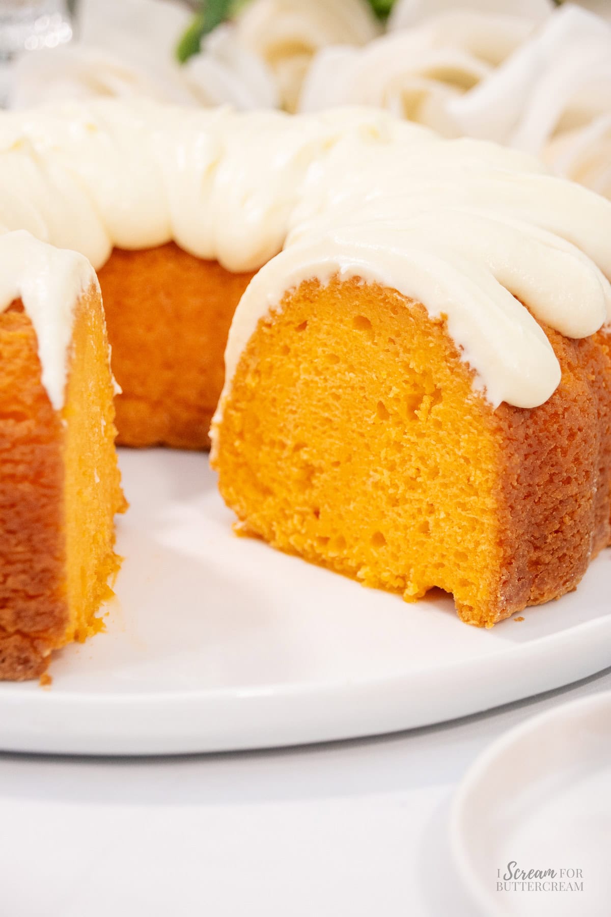 A close-up of a moist orange bundt cake with thick cream cheese frosting, showing a slice removed to reveal its vibrant interior.