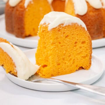 A slice of orange creamsicle bundt cake with white frosting sits on a plate with a fork holding a bite-sized piece in the foreground.