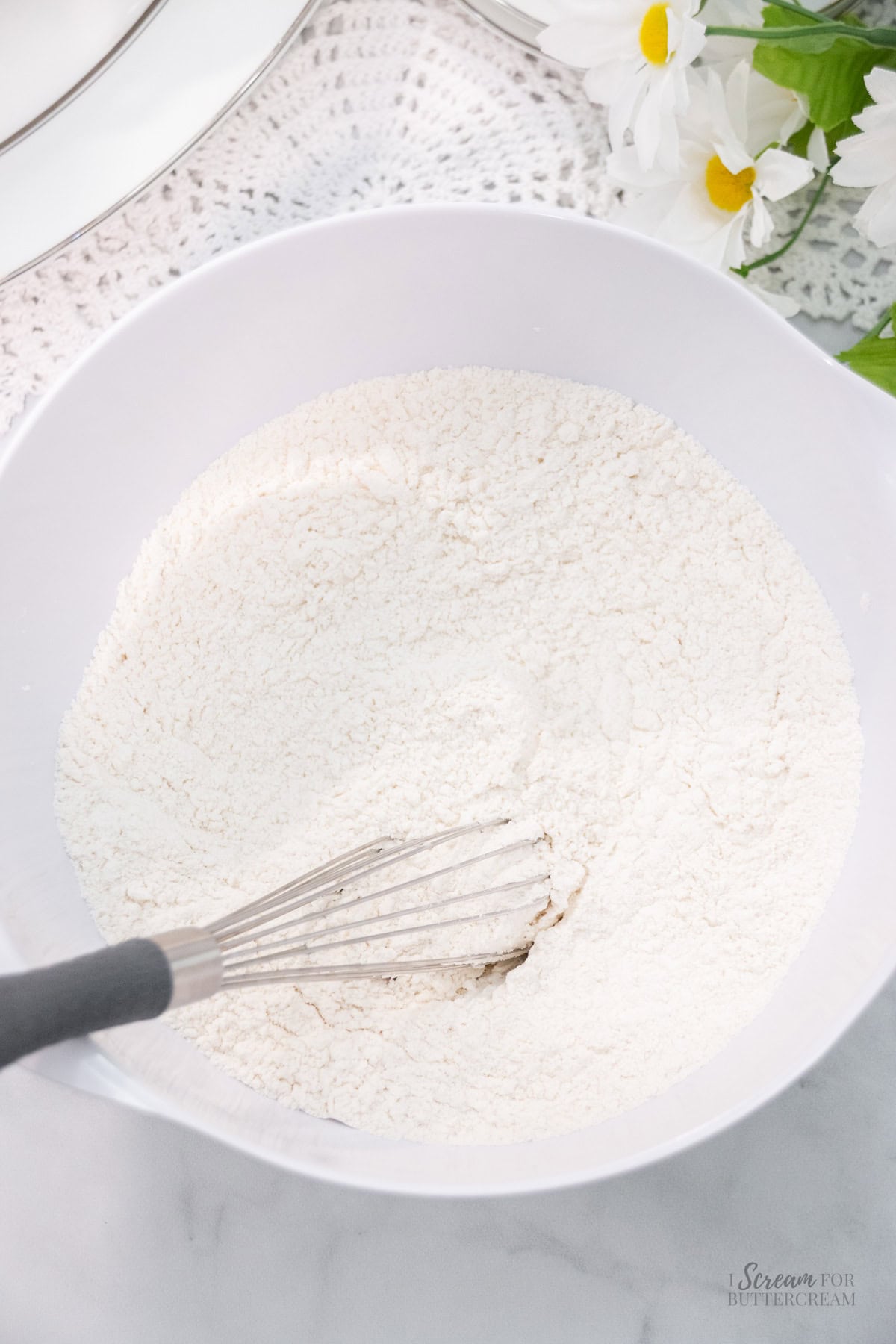 Dry cake ingredients being whisked in a white mixing bowl.