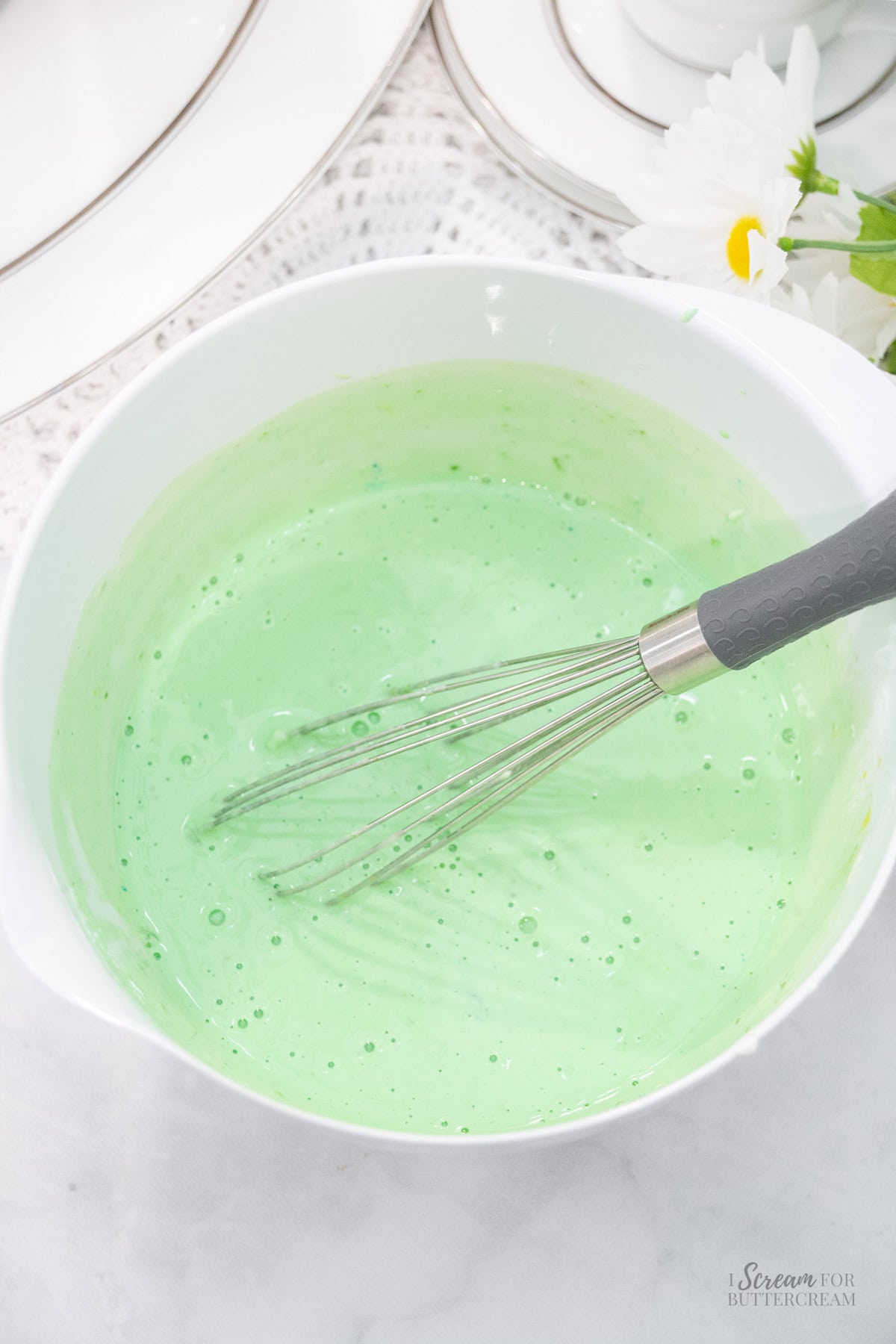 Smooth, light green key lime cake batter in a white bowl with a whisk.