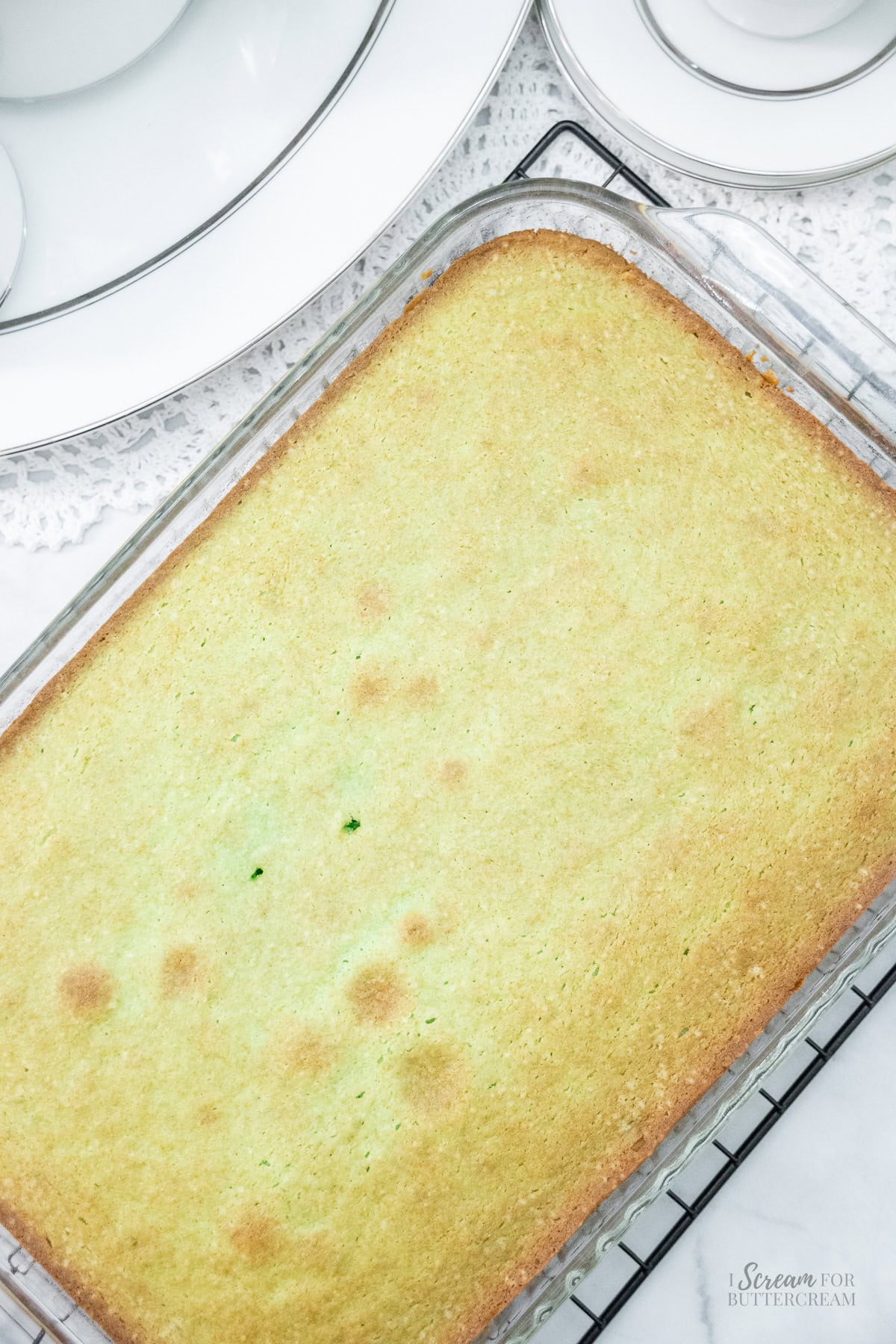 Freshly baked key lime cake in a glass pan with a golden top and hints of green peeking through.
