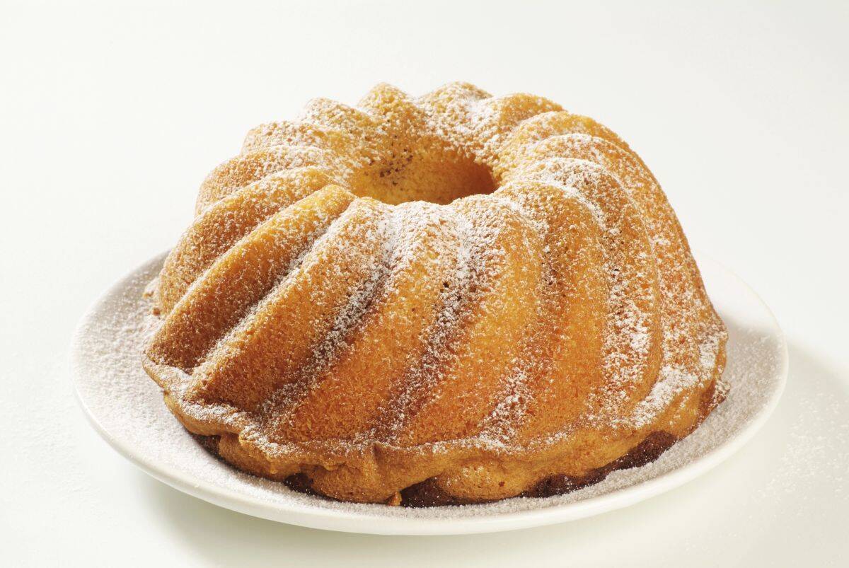 A classic golden bundt cake dusted with powdered sugar, served on a white plate with a clean, minimal background. The cake's defined ridges and light coating of sugar give it a simple yet elegant look.
