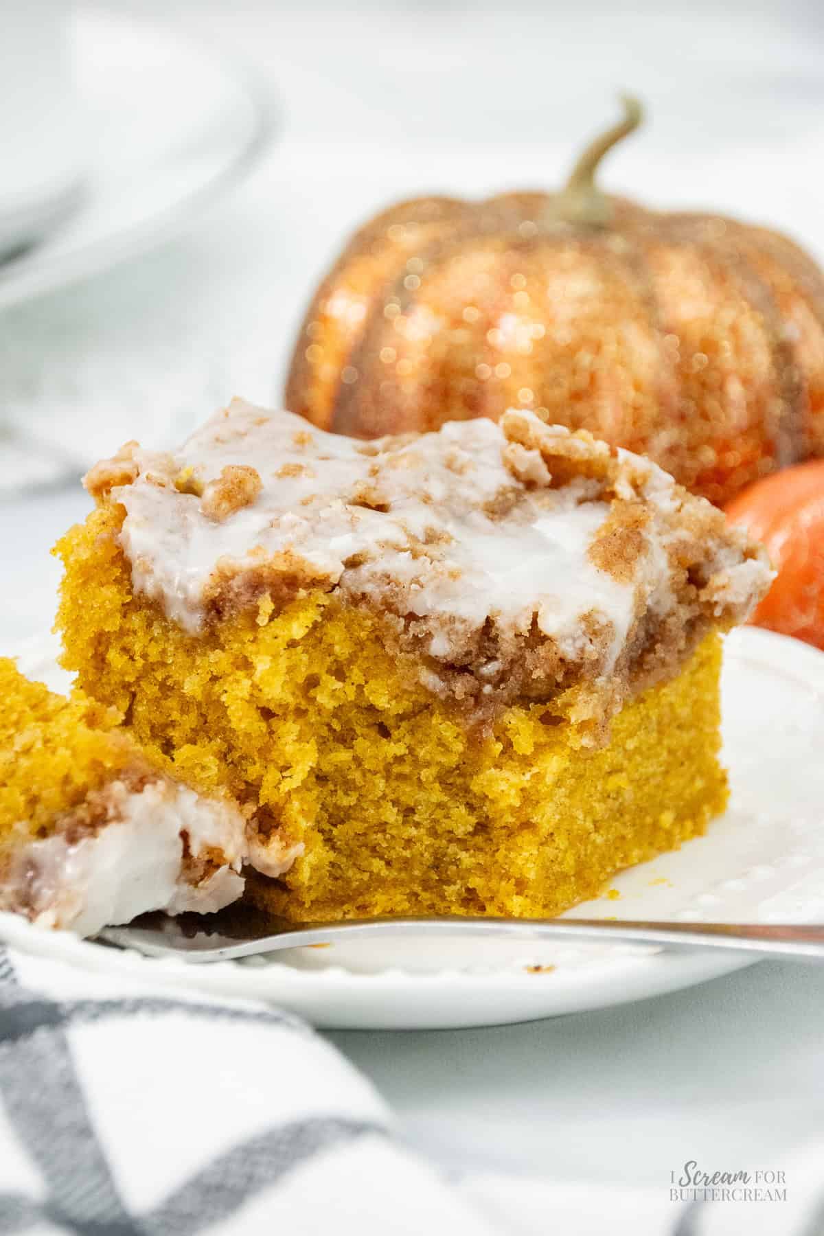 A slice of pumpkin coffee cake with a thick cinnamon streusel and vanilla glaze, served on a white plate with a fork and decorative glitter pumpkins in the background.