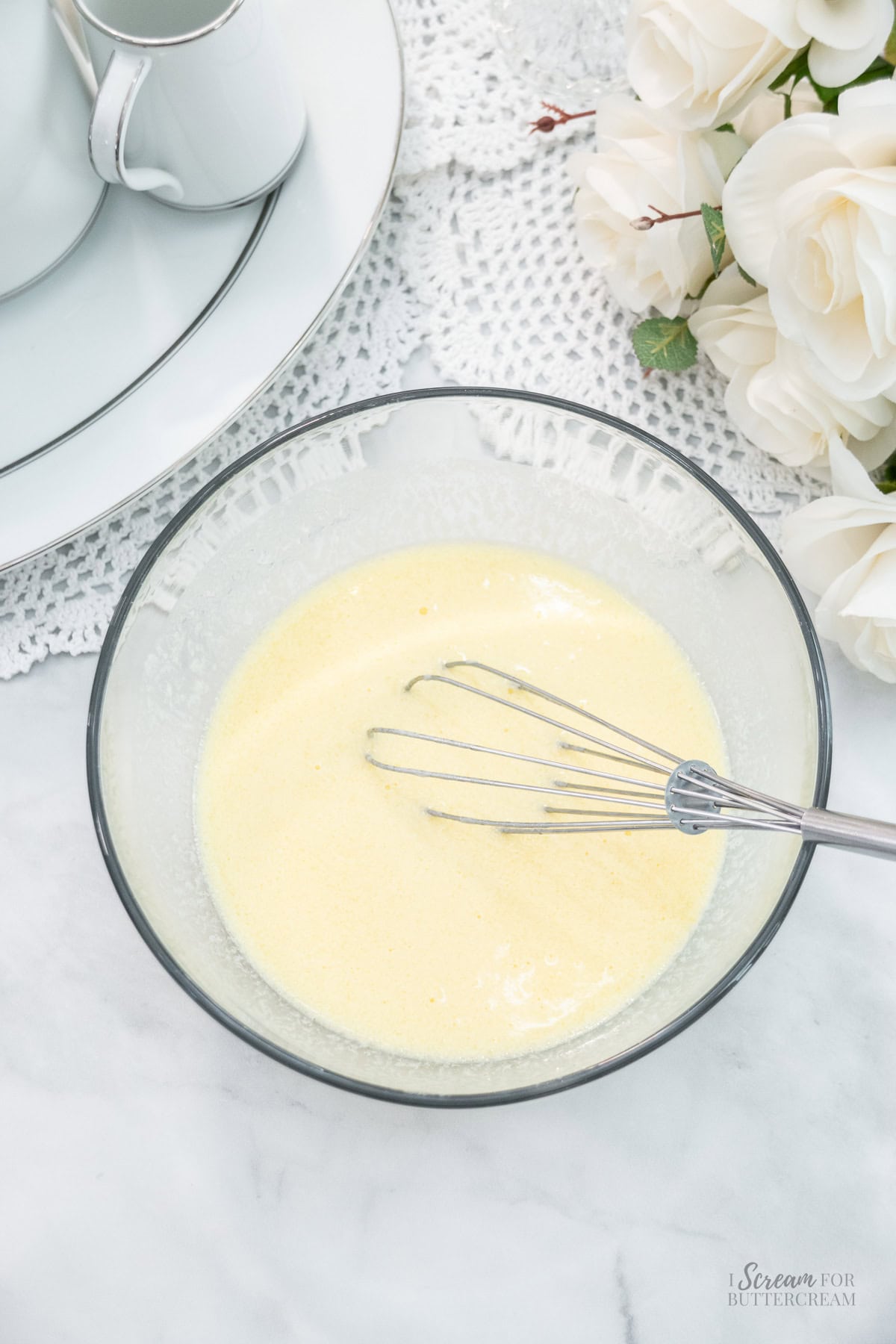 Glass bowl filled with a liquid cake batter mixture and a metal whisk resting inside.