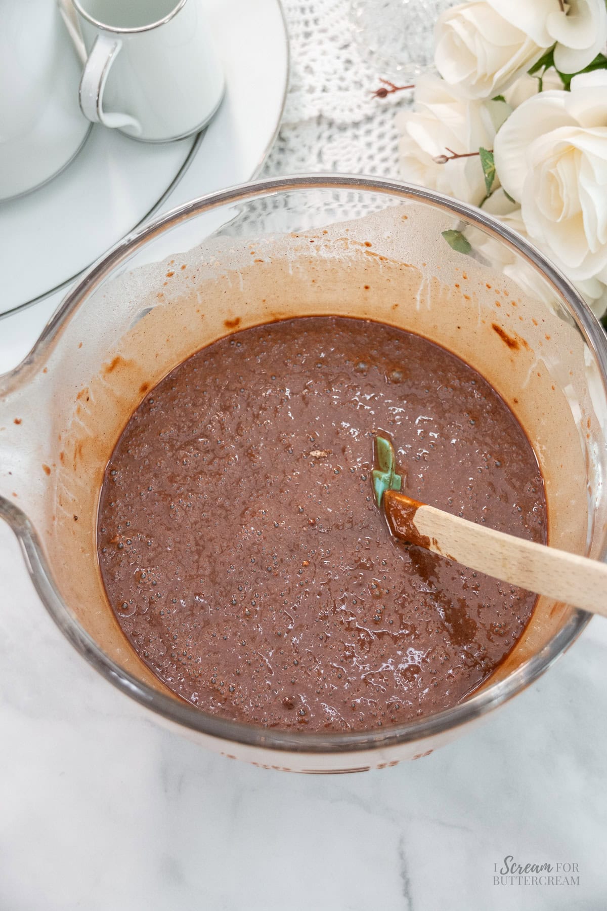 Glass mixing bowl filled with chocolate cake batter, with a spatula resting inside.