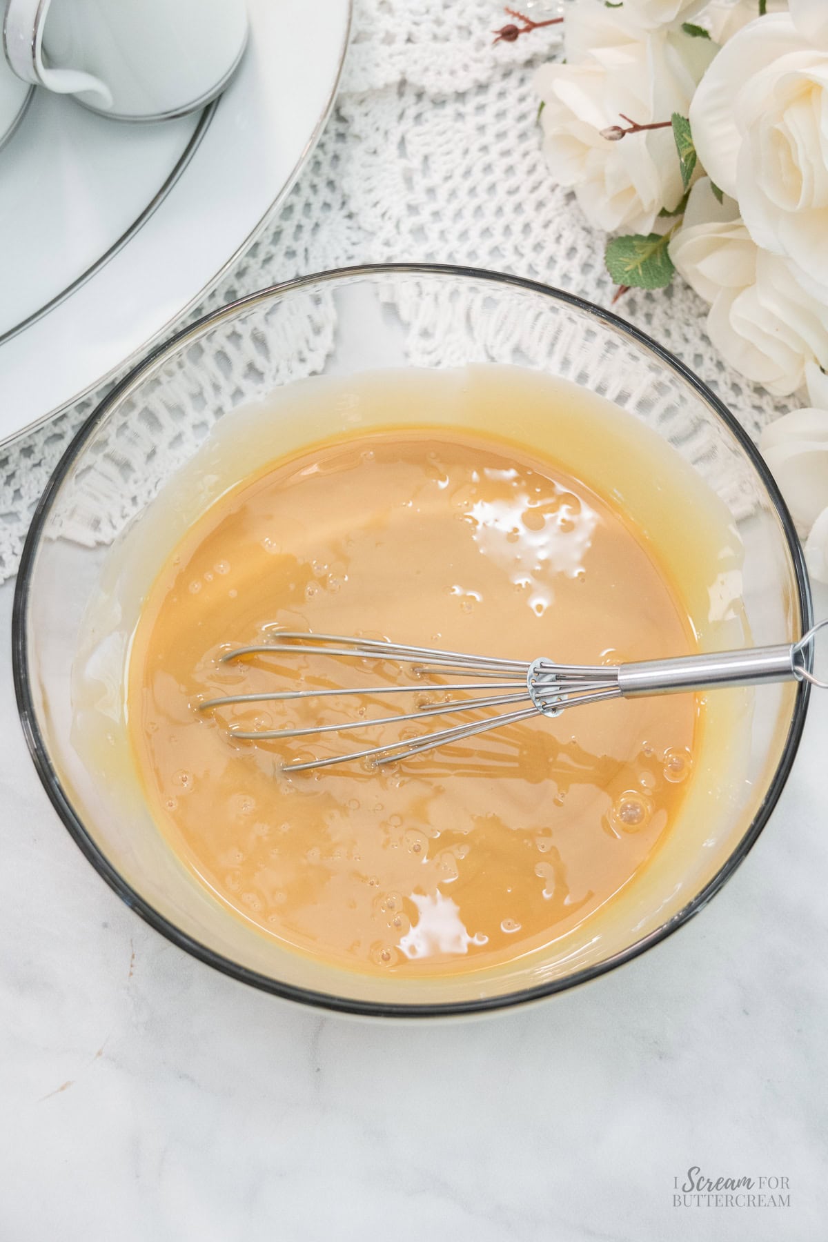 Glass bowl with sweetened condensed milk and caramel mixture being whisked together.