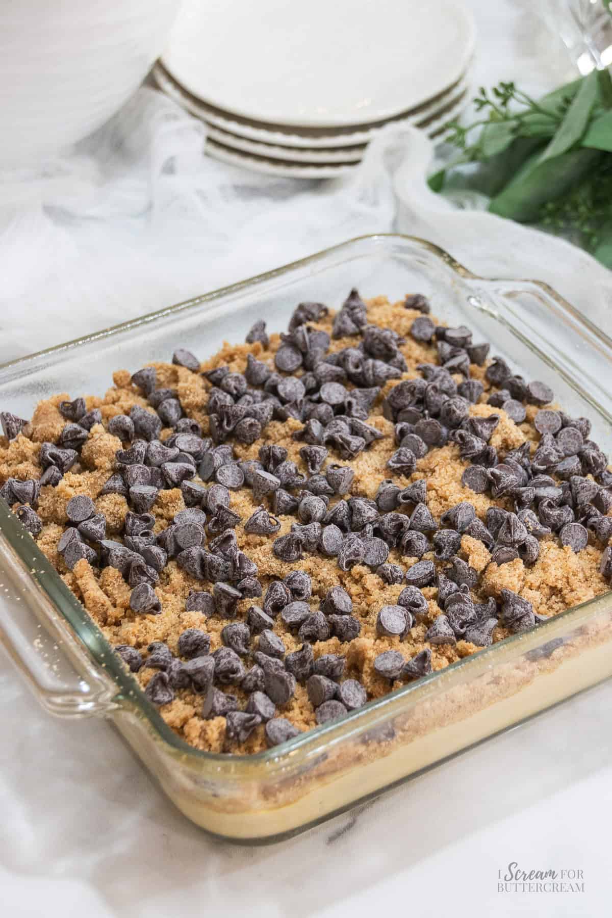 Chocolate chip coffee cake in a glass baking dish topped with cinnamon crumb topping and chocolate chips before baking.