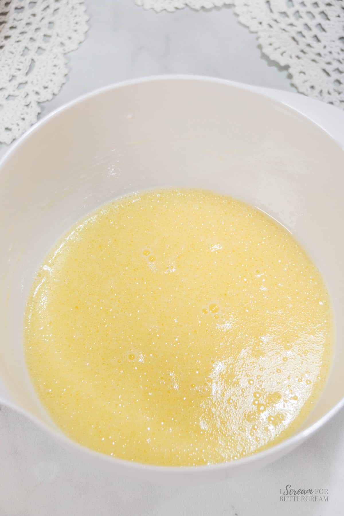 Eggs and sugar beaten together in a mixing bowl until light, smooth, and slightly foamy.